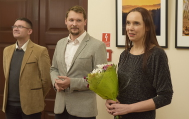 Dwoje mężczyzn i kobieta. Kobieta z kwiatami opowiada o Galerii