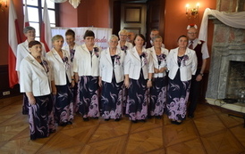 Klub seniora pozujący do zdjęcia w dw&oacute;ch rzędach przed dekoracją patriotyczną