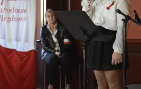 Dziewczyna w okularach recytuje wiersz, za nią siedzi zamyślona kobieta