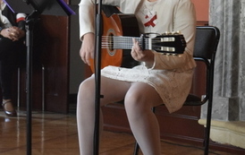 Dziewczynka w białej sukience gra na gitarze i śpiewa