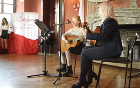 Dziewczynka z nauczycielką grają na gitarach i śpiewają piosenkę.