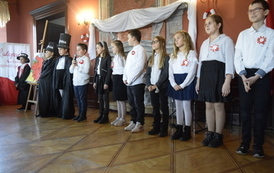 Uczniowie szkoły podstawowej w galowych strojach przedstawiają inscenizację 