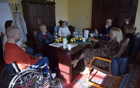 Grupa ludzi siedzi przy stole. Jeden mężczyzna siedzi na w&oacute;zku inwalidzkim.