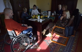 Grupa ludzi siedzi przy stole. Jeden mężczyzna na w&oacute;zku inwalidzkim.