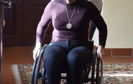 Dwie kobiety. Jedna jedzie na w&oacute;zku inwalidzkim. Druga pochylona pcha w&oacute;zek.