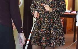 Kobieta w goglach wchodzi do pomieszczenia. w ręce trzyma białą laskę i coś m&oacute;wi.