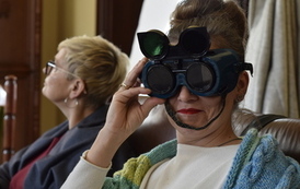 Kolejna kobieta w goglach patrzy na wprost. na drugim planie druga kobieta patrzy w dal.