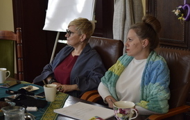 Dwie kobiety siedzą przy stole. obie patrzą w jednym kierunku.